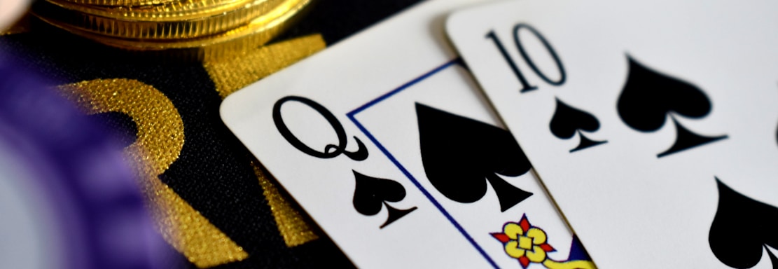 A close-up view of playing cards, specifically a Queen and a Ten of spades, surrounded by shiny gold coins and part of a poker chip, suggesting a gambling or casino theme.