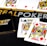 Poker-themed setup featuring a deck of cards on a table with the words 'REAL POKER' visible. Two cards, the King of Clubs and Jack of Diamonds, are prominently displayed. The design is vibrant, with detailed illustrations on the cards.