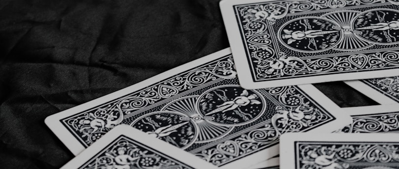 A pile of playing cards featuring intricate, symmetrical patterns on their backs, placed on a dark surface.