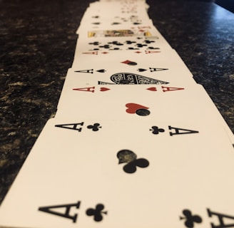 A line of playing cards arranged in a perspective view across a dark marbled surface, prominently featuring aces of clubs and hearts.