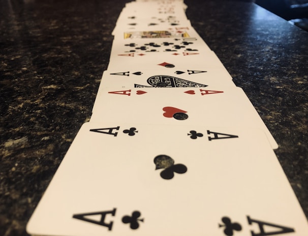 A line of playing cards arranged in a perspective view across a dark marbled surface, prominently featuring aces of clubs and hearts.